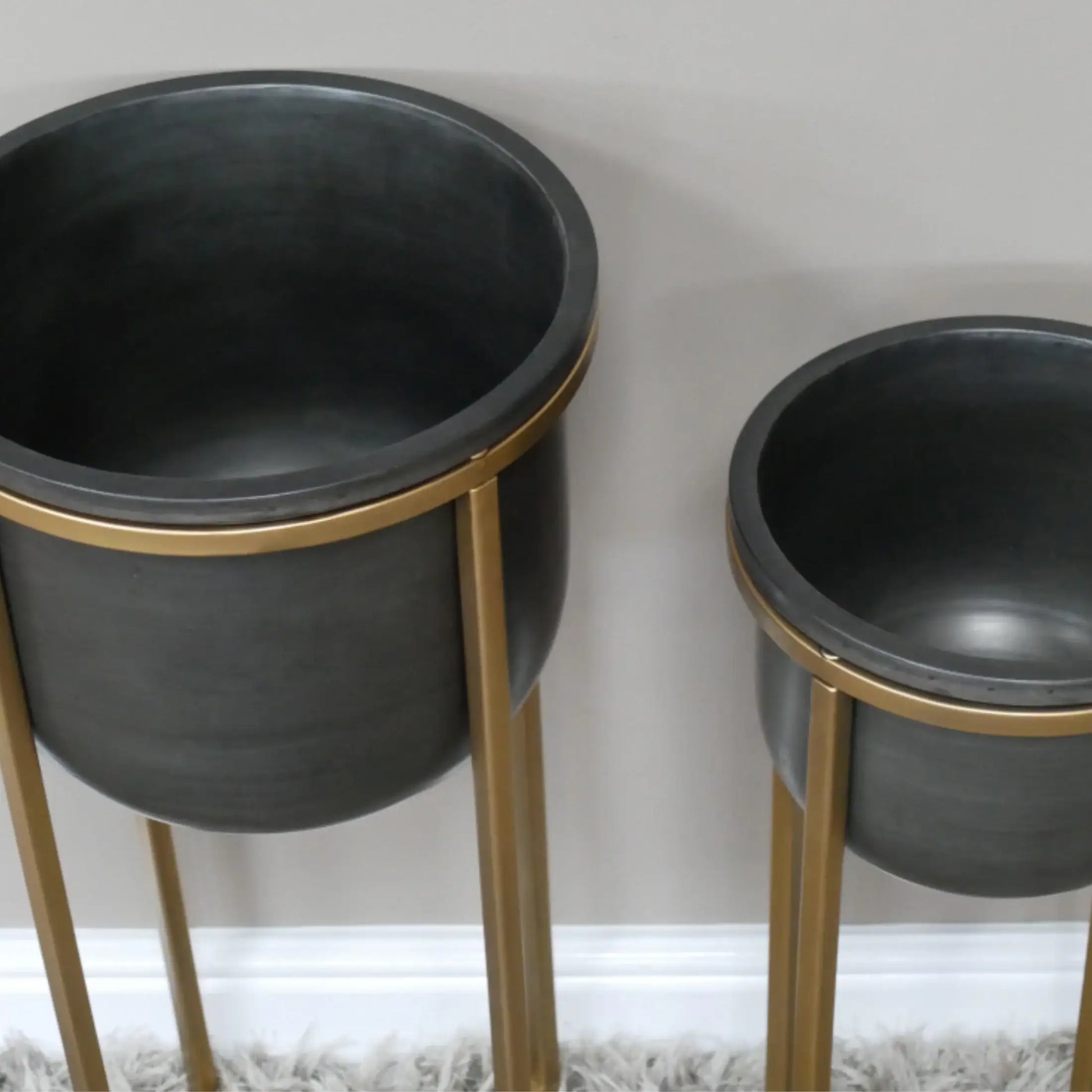 Two black planters with gold stands on a neutral background