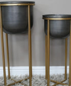 Two black planters on gold stands against a gray wall.