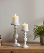 Two white candles in decorative candle holders on a table with a neutral background