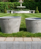 Two concrete planters on grass with a fountain in the background