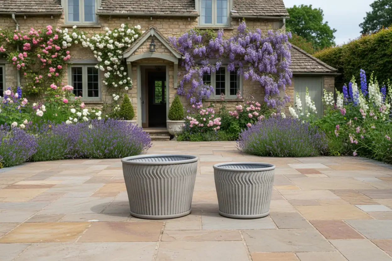 Two gray planters on a stone patio with a garden and house in the background