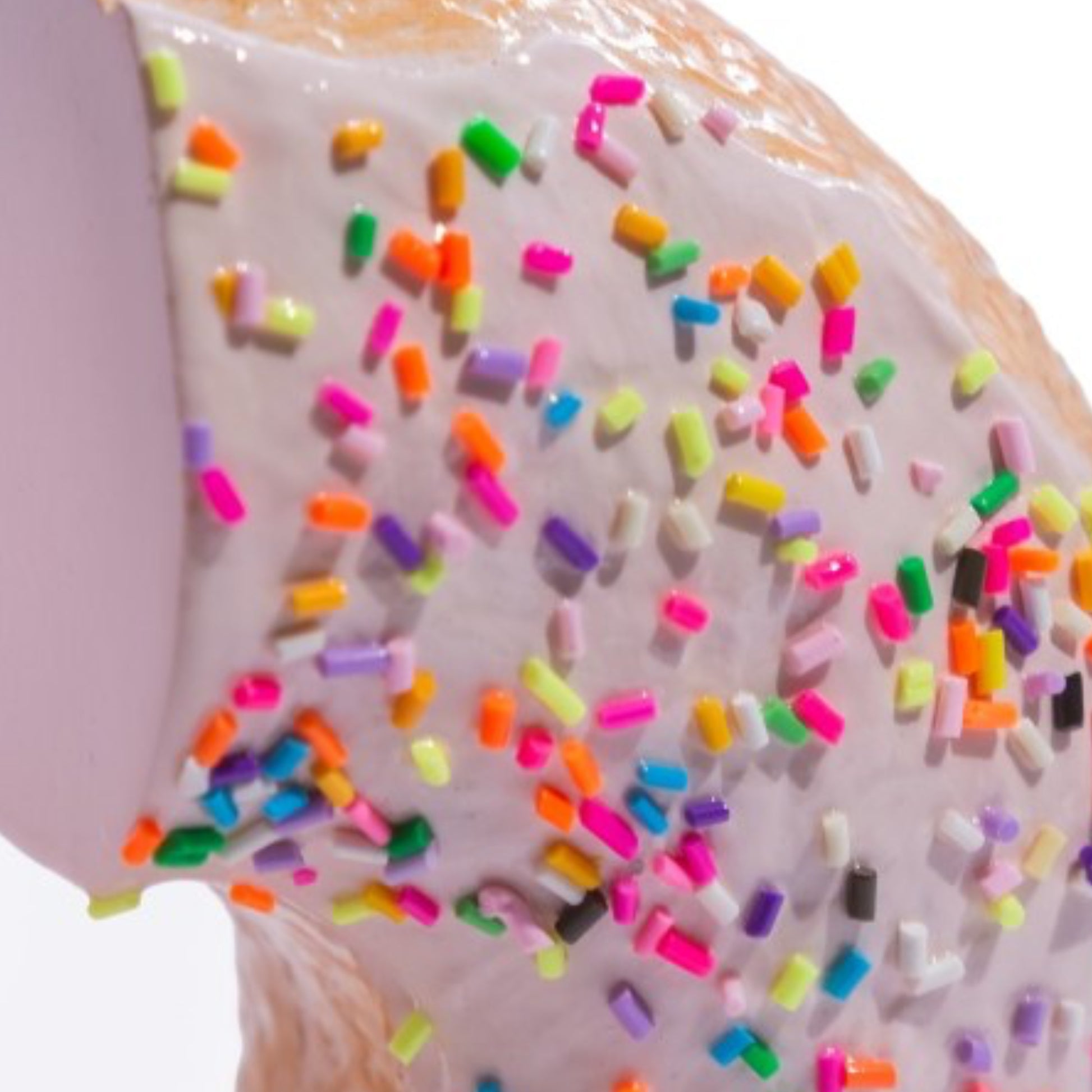 A close-up of a donut or pastry with pale pink icing and scattered rainbow sprinkles, photographed against a white background.