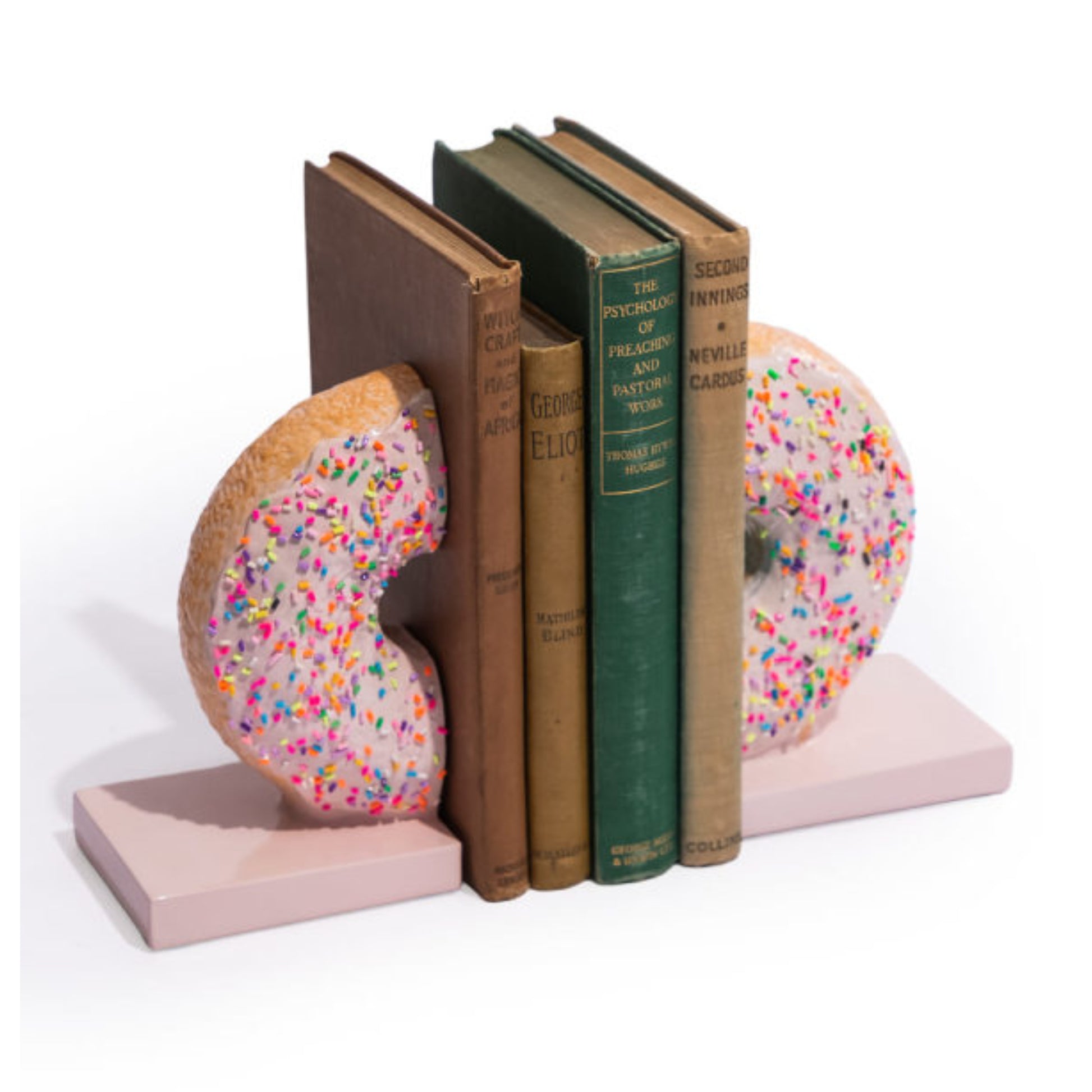 A pair of novelty donut-shaped bookends holding up a row of vintage-style books on a clean white background. The bookends are light pink with raised donut shapes covered in multicolored sprinkles, and the books in between add brown, green, and tan tones.