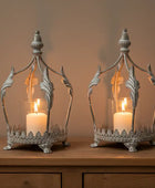 Two ornate metal candle holders with lit candles on a wooden surface.