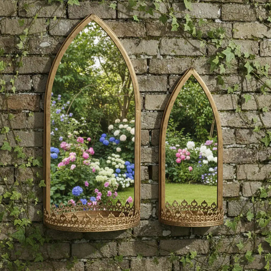 Two ornate mirrors on a stone wall reflecting a garden with flowers.