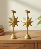 Two gold star-shaped candle holders on a wooden surface with books and a plant in the background.