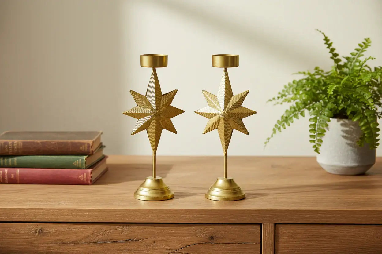 Two gold star-shaped candle holders on a wooden surface with books and a plant in the background.
