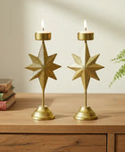 Two gold star-shaped candle holders on a wooden surface with books and a plant in the background.