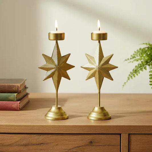 Two gold star-shaped candle holders on a wooden surface with books and a plant in the background.