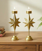 Two gold star-shaped candle holders on a wooden surface with books and a plant in the background.