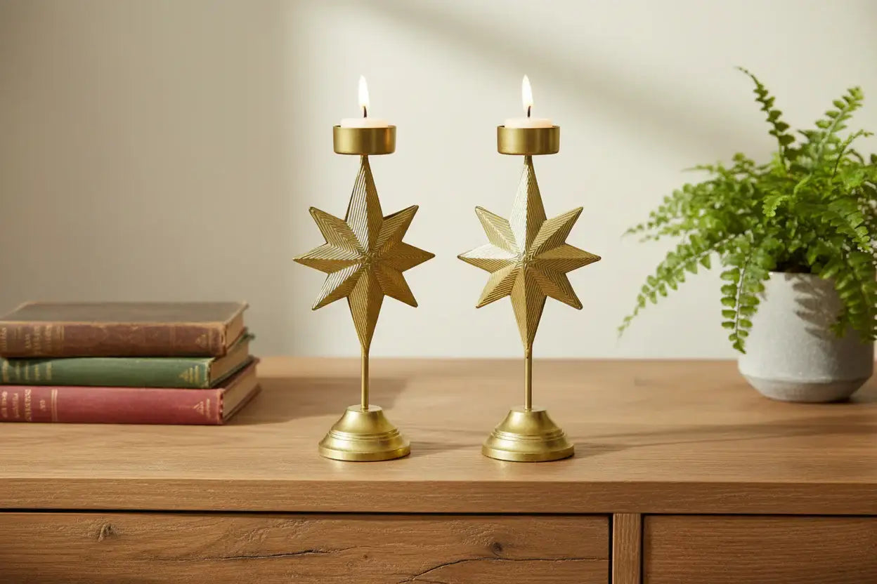 Two gold star-shaped candle holders on a wooden surface with books and a plant in the background.