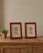 Two red-framed silhouettes on a wooden surface with a plant and book in the background.