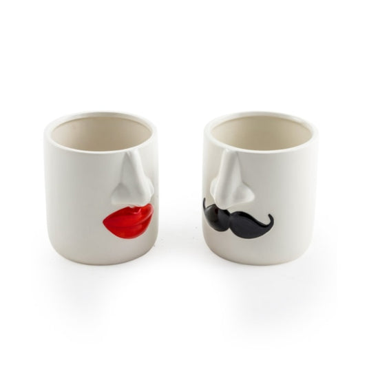 Two white ceramic novelty cups shaped like faces, one with red lips and one with a black mustache, on a white background.