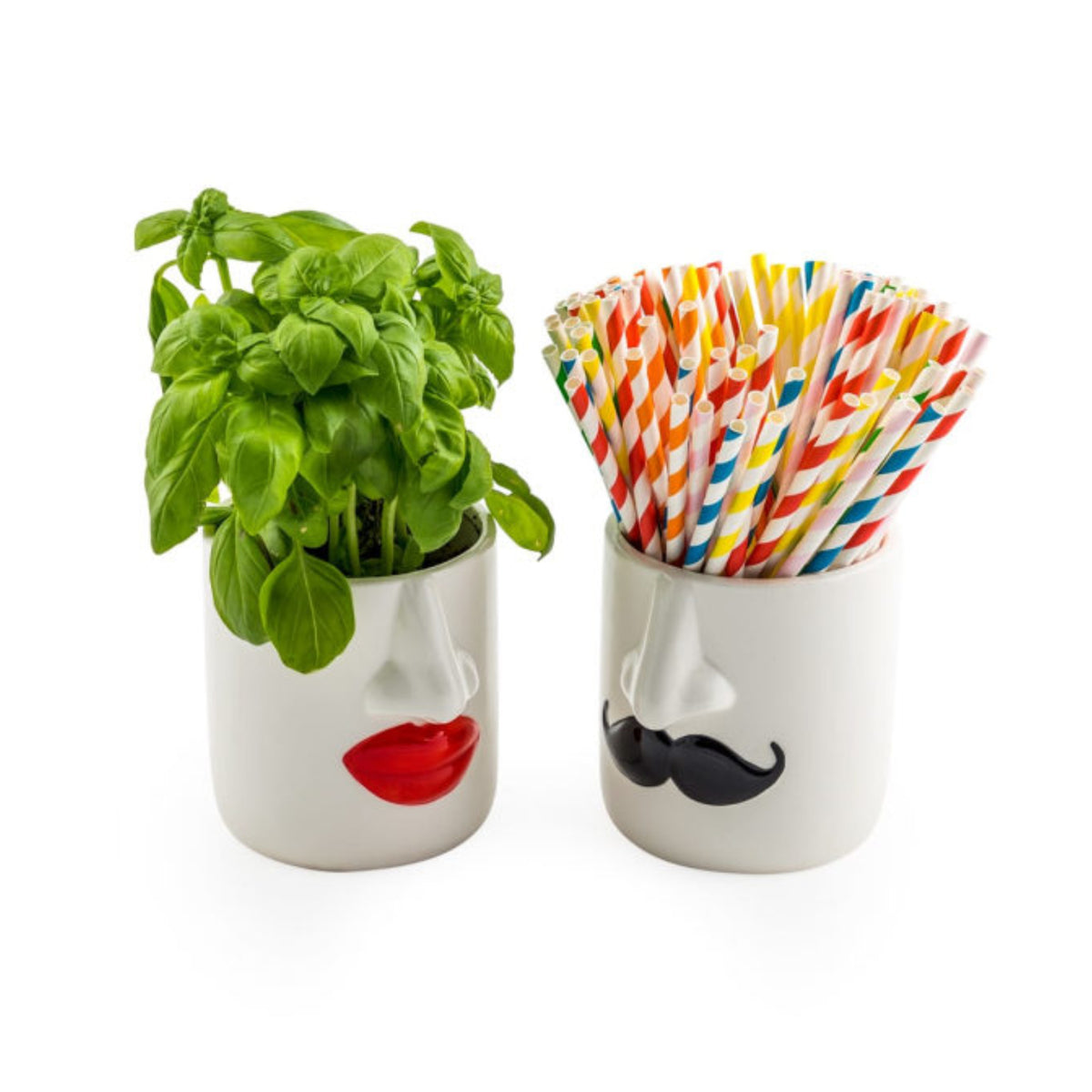 Two white ceramic cups shaped like stylized faces, one with red lips holding a green basil plant and the other with a black mustache holding a set of colorful striped paper straws, on a white background.