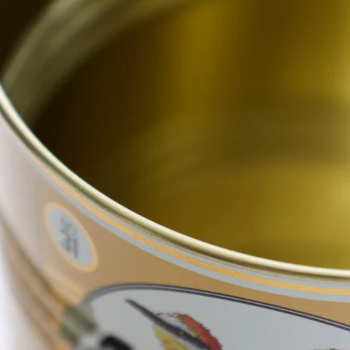 Close-up of the interior of a gold-colored metal tin can with a partially visible label featuring a fish illustration.
