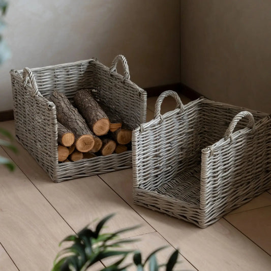 Two wicker baskets on a wooden floor with one containing logs.
