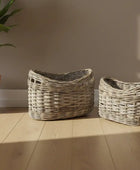 Two wicker baskets on a wooden floor with a plant in the background.