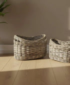 Two wicker baskets on a wooden floor with a plant in the background