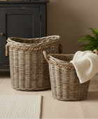 Two woven baskets with a knit blanket on a wooden floor next to a cabinet.