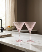 Two pink fluted martini glasses on a white marble kitchen counter in a modern kitchen setting.