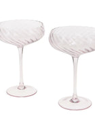 Two pale pink champagne coupe glasses with a ribbed, textured bowl and slender stems, shown on a plain white background.
