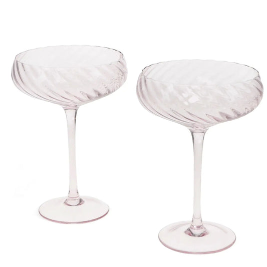 Two pale pink champagne coupe glasses with a ribbed, textured bowl and slender stems, shown on a plain white background.