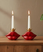 Red lip-shaped candle holder with a white candle on a wooden surface next to a plant.