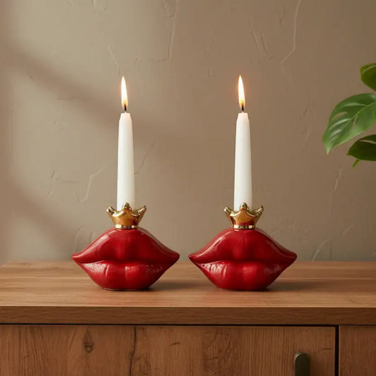 Red lip-shaped candle holder with a white candle on a wooden surface next to a plant.