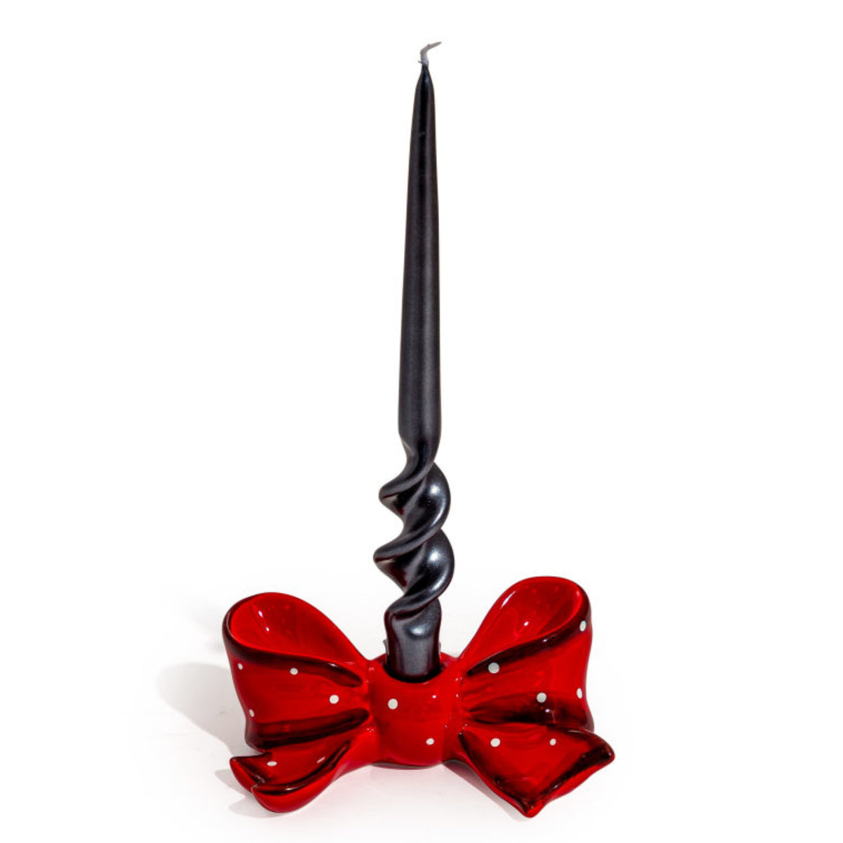 A black taper candle with a spiral twist base, set in a glossy red bow-shaped holder with white polka dots, on a plain white background.