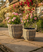 Wicker planters with flowers on a stone patio in front of a house with floral decorations.