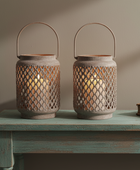 Two rustic metal lantern candles with wire diamond-pattern cutouts and arched handles, placed on a distressed teal table against a warm beige wall.