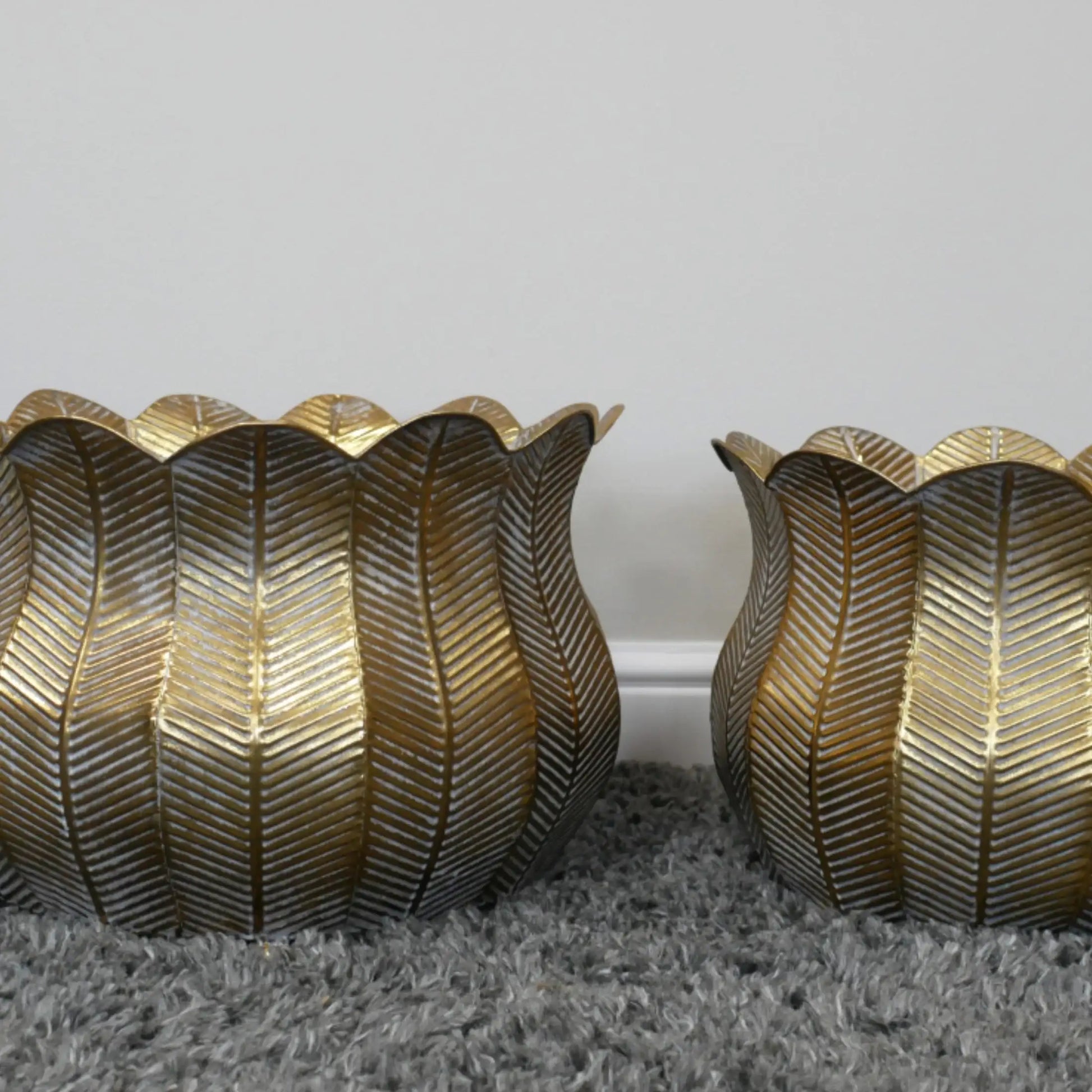 Two gold leaf-patterned candle holders on a gray surface with a white background