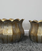 Two gold leaf-patterned candle holders on a gray surface with a white background