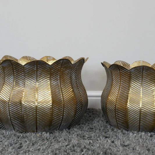 Two gold leaf-patterned candle holders on a gray surface with a white background