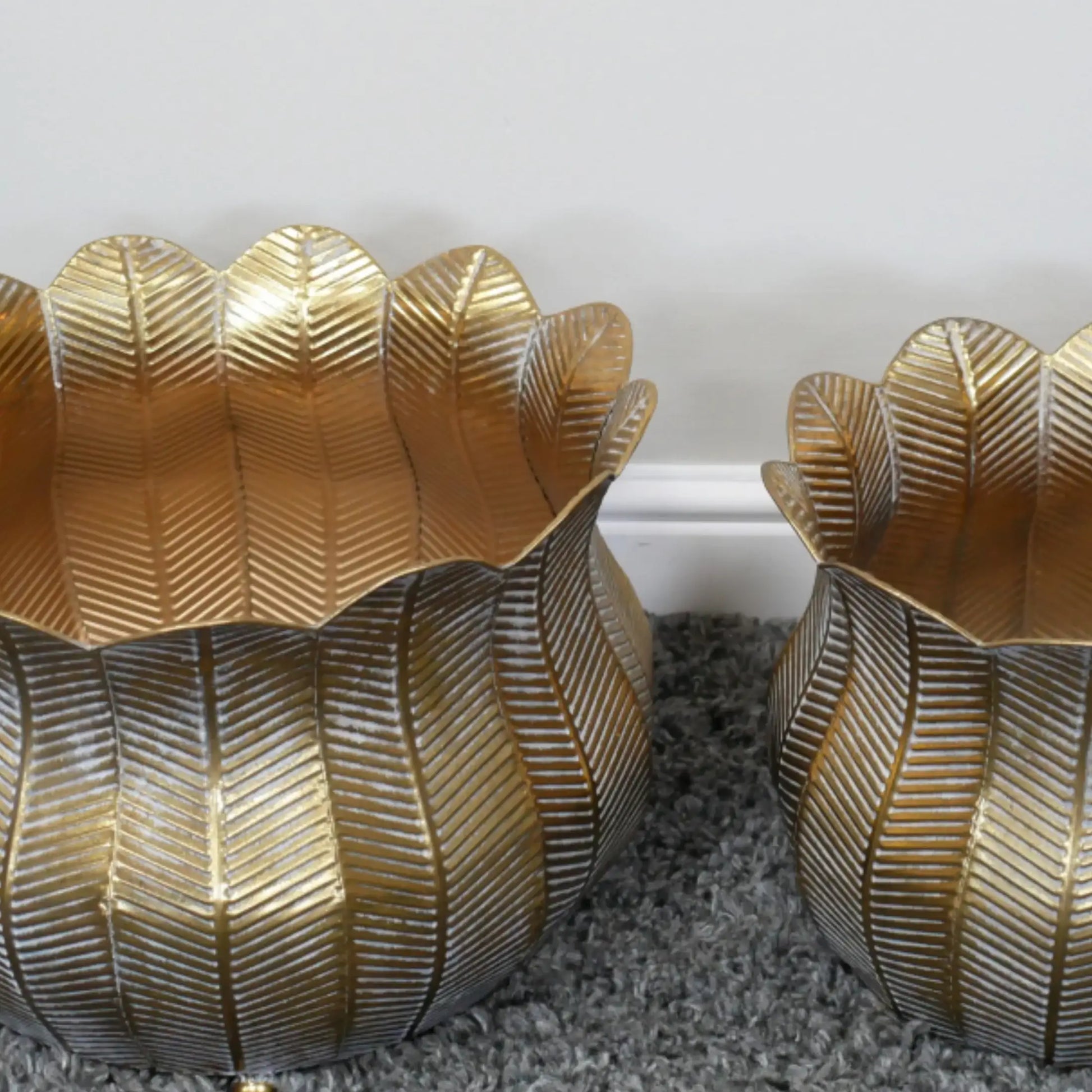 Two gold leaf-patterned candle holders on a textured surface.