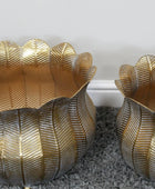 Two gold leaf-patterned candle holders on a textured surface.
