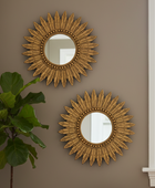 Two decorative gold sunburst mirrors mounted on a taupe wall, with a green fiddle-leaf fig plant on the left and a white window frame on the right.