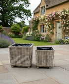 Two wicker planters on a stone patio with a garden and house in the background