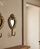 Two ornate gold wall hooks with heart-shaped mirrors, mounted on a beige wall next to an open doorway.