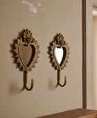 Two ornate gold wall hooks shaped like sunburst hearts with mirror centers, mounted on a beige wall.