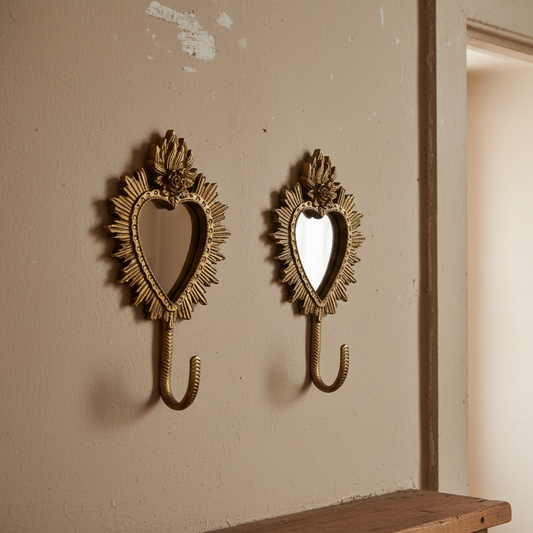 Two ornate gold wall hooks shaped like sunburst hearts with mirror centers, mounted on a beige wall.