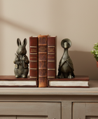 Two decorative bookends shaped like a rabbit and a duck, each mounted on a faux leather book and flanking a set of three vintage-style brown books on a gray wooden console table.