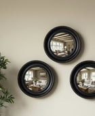 Three round black-framed mirrors on a beige wall with a plant to the left.