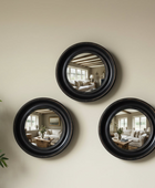 Three round black-framed mirrors on a beige wall reflecting a living room.