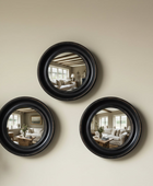 Three round black-framed mirrors on a beige wall reflecting a living room.