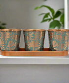 Three decorative metal pots with floral patterns on a matching tray.
