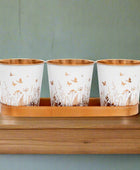 Three white cups with gold floral patterns on a wooden tray against a white background