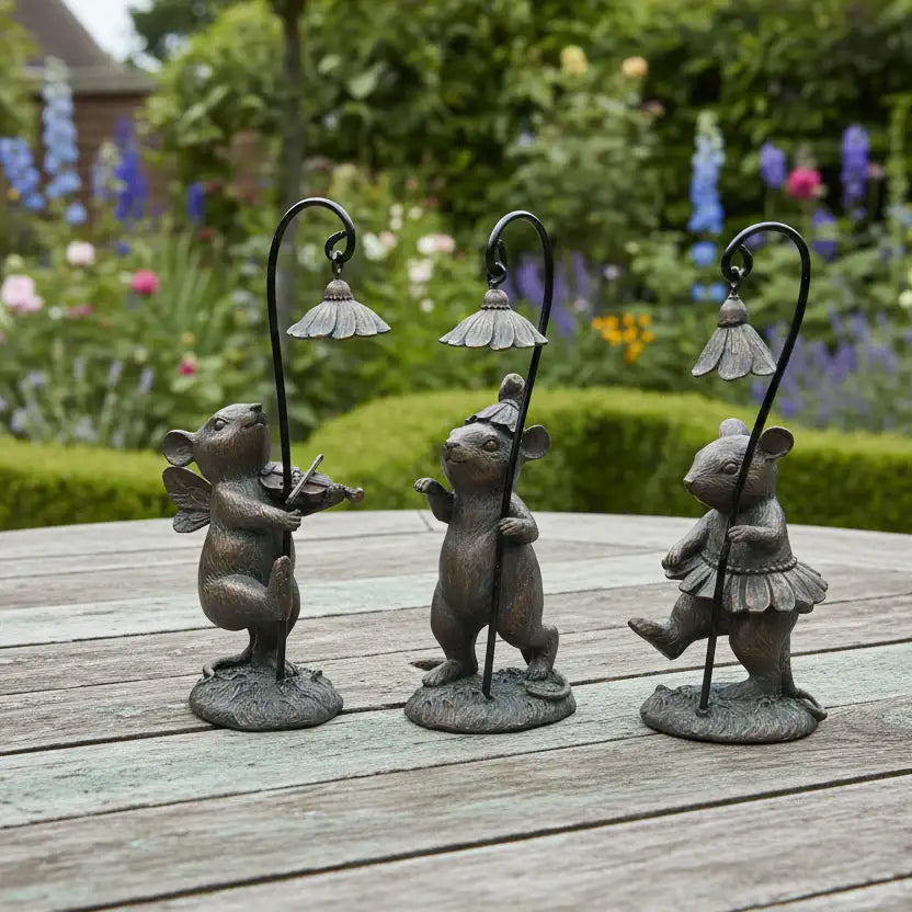 Three decorative mouse statues with lampshades on a wooden surface with a garden background.