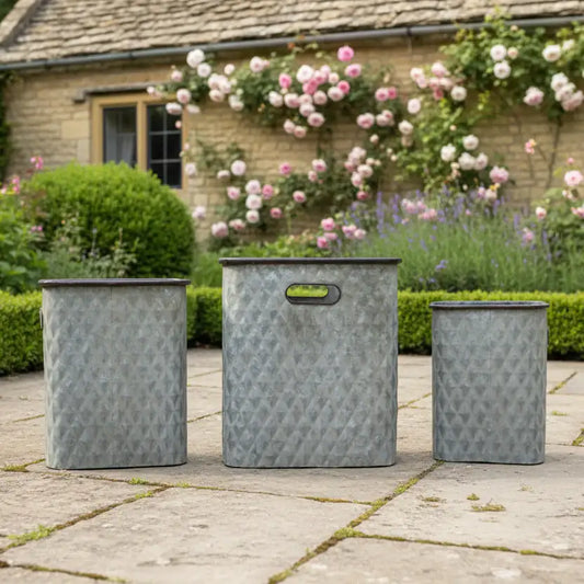 Three metal planters on a patio with a garden and house in the background