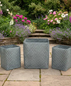 Three gray woven planters on a stone patio with a garden in the background